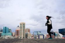 A woman jogs with the Baltimore skyline behind her.
