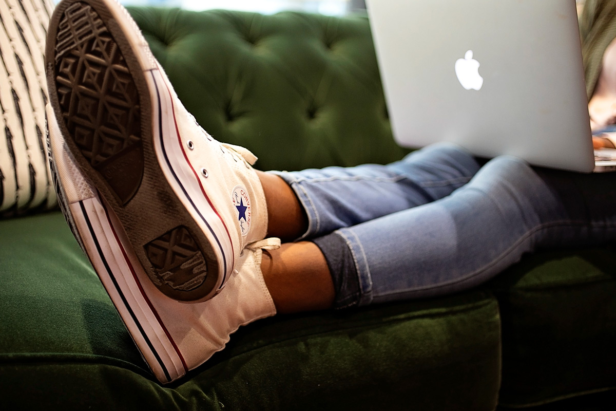 A person works on a laptop while wearing white converse shoes.