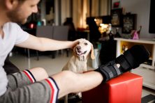 A man with a fractured leg pets his dog at home.