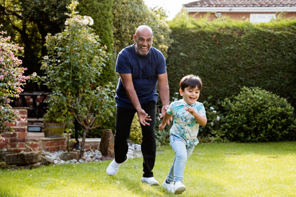 A grandfather runs after his grandchild in his backyard.