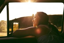 A woman looks out the car window while smiling.