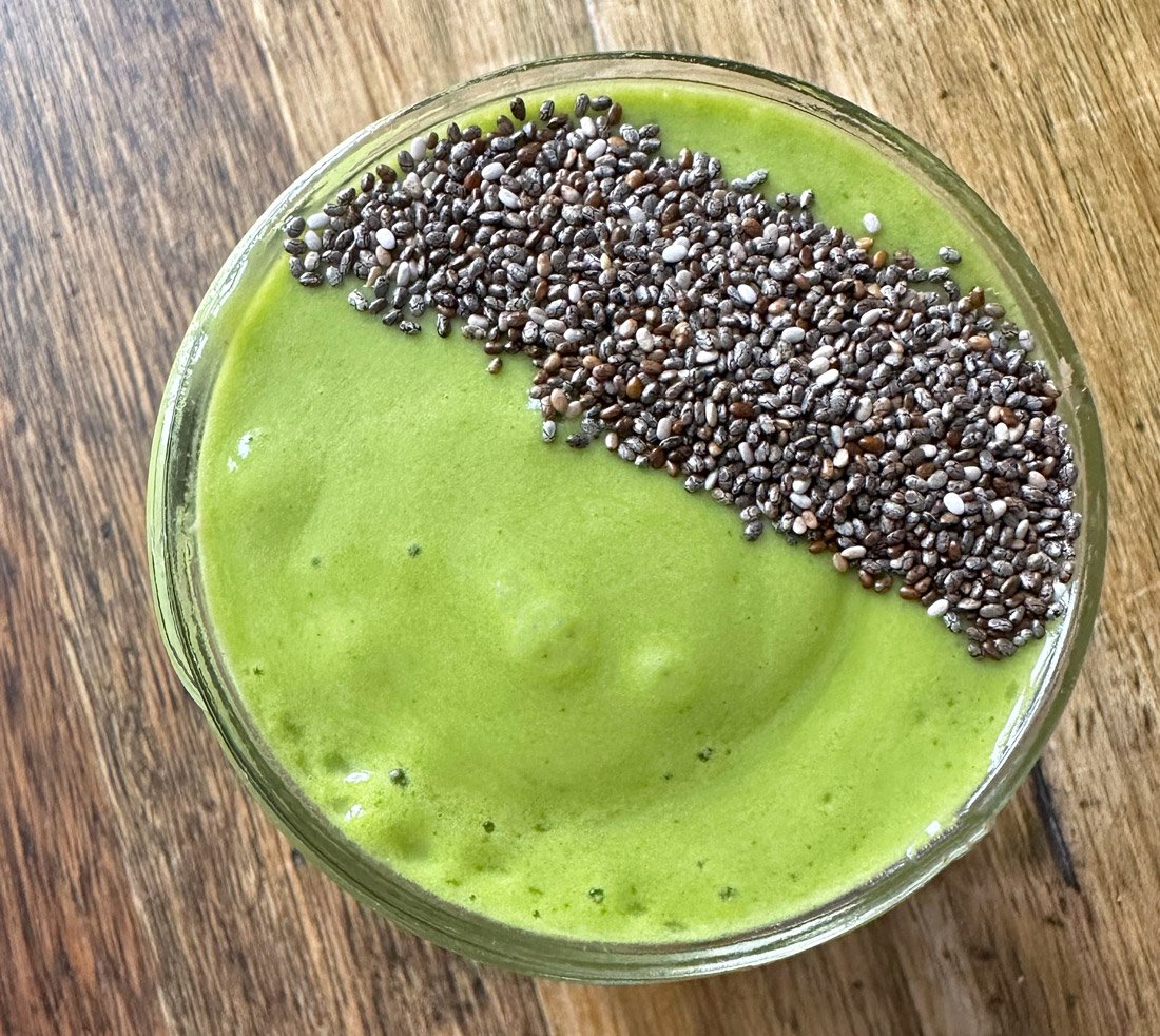 An arugula mango smoothie with chia seeds on top sit in a cup to drink.