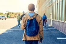 A man wearing a book bag walks.