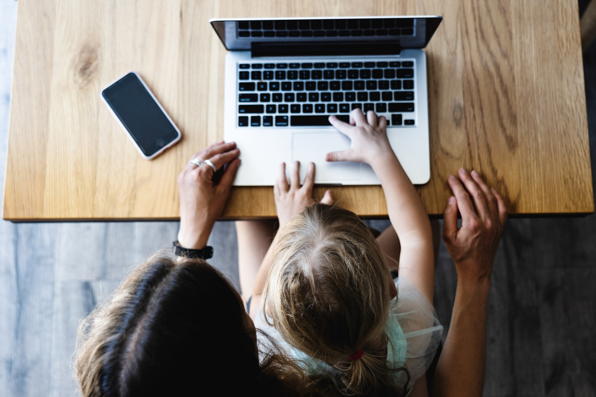 A mother works on her laptop as her child sits on her lap trying to type on the keyboard. 