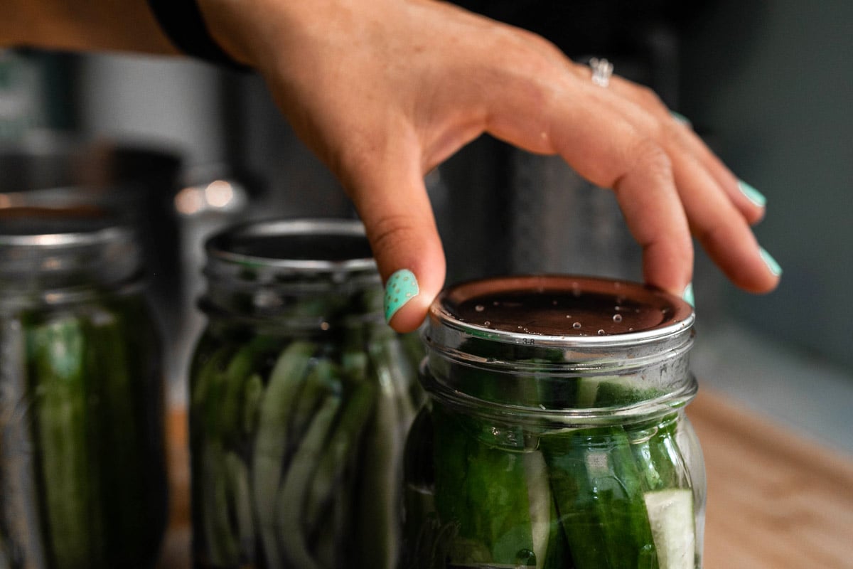 A person screws on the lid to a mason jar. Inside the jar are pickled vegetables.