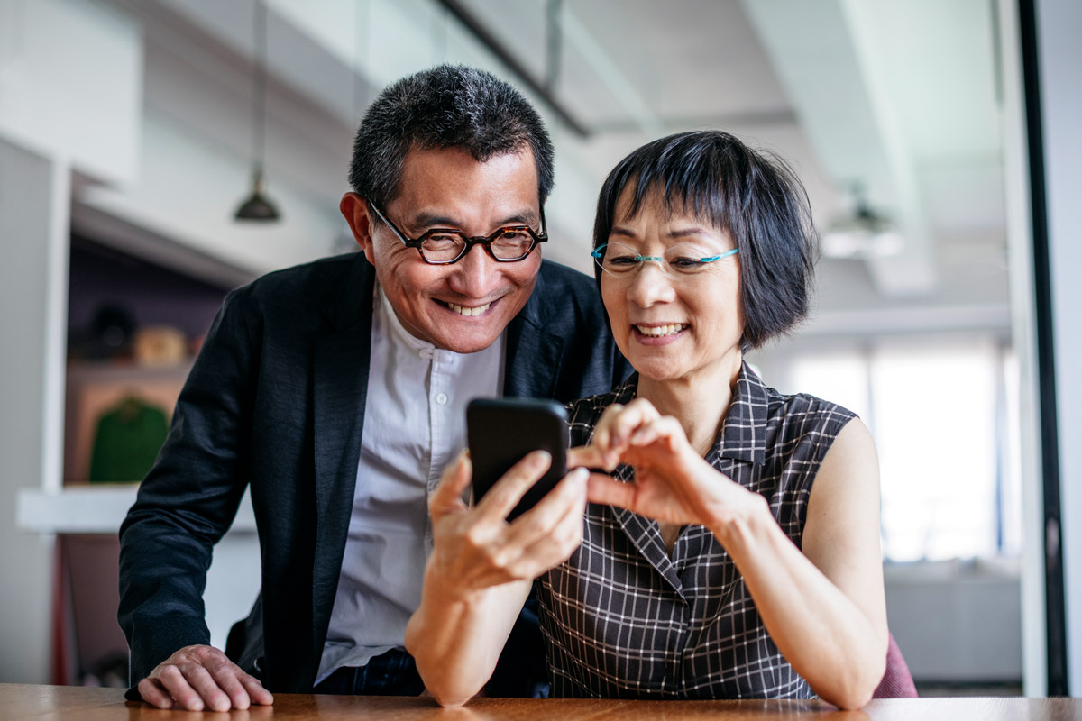 A mature husband and wife smile as they look at their phone.