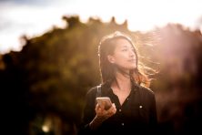 A woman holds a phone as she looks off into the distance with her hair blowing in the wind. This story goes over if it's a good time to invest.