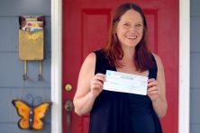 A woman poses with a check against her red door.