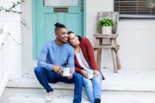 New home owners look off into the distance as they sit on their front porch and drink coffee.