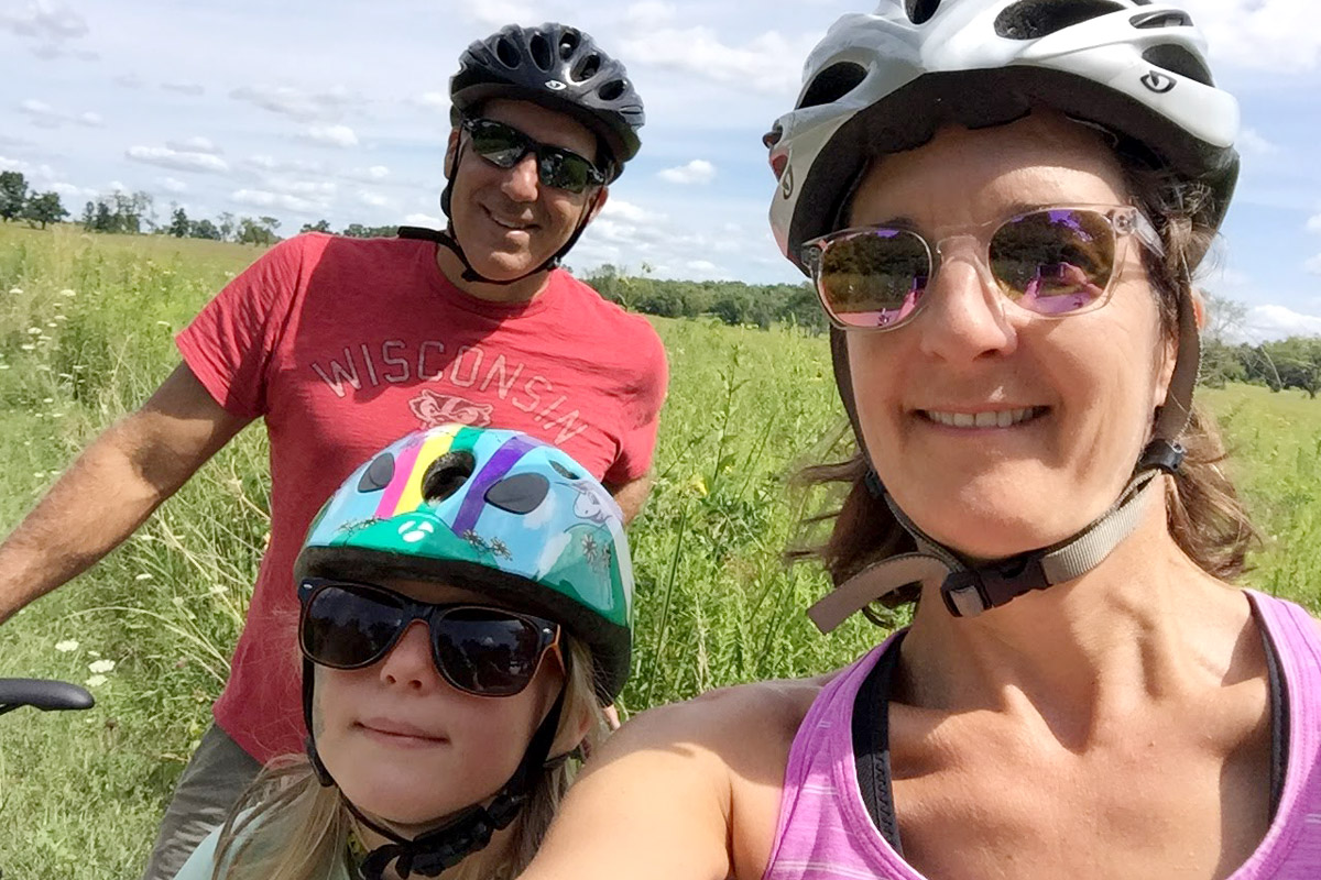 This photo shows a family taking a selfie while taking a break from a bicycle ride against a field of grass. 