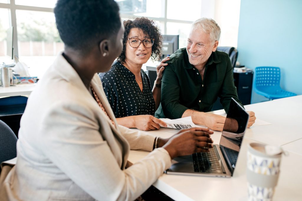 A person working for a bank talks to two customers while sitting down at a desk. Signing up with Associated Bank Balanced Checking could save you up to $500.