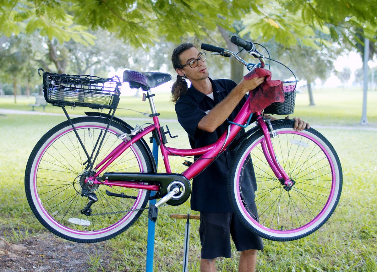 A man wipes down a bicycle in a park. 