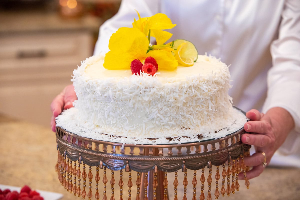 A woman shows off a homemade cake she made. She decorated it with fresh fruit. 