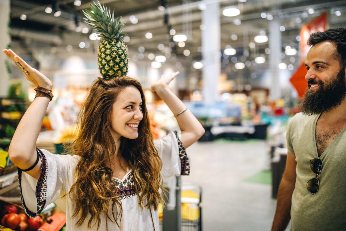 A woman balances a pineapple on her head while at the grocery store. 