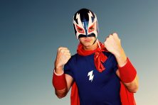 A luchador poses for a photo with his hands up in the air.