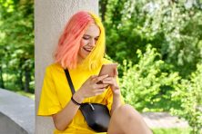 A woman with pink and yellow hair as a happy expression on her face when looking at her phone.