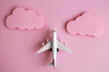 A toy plane lays on pink paper to show it going up in the sky with pink clouds in this photo illustration.