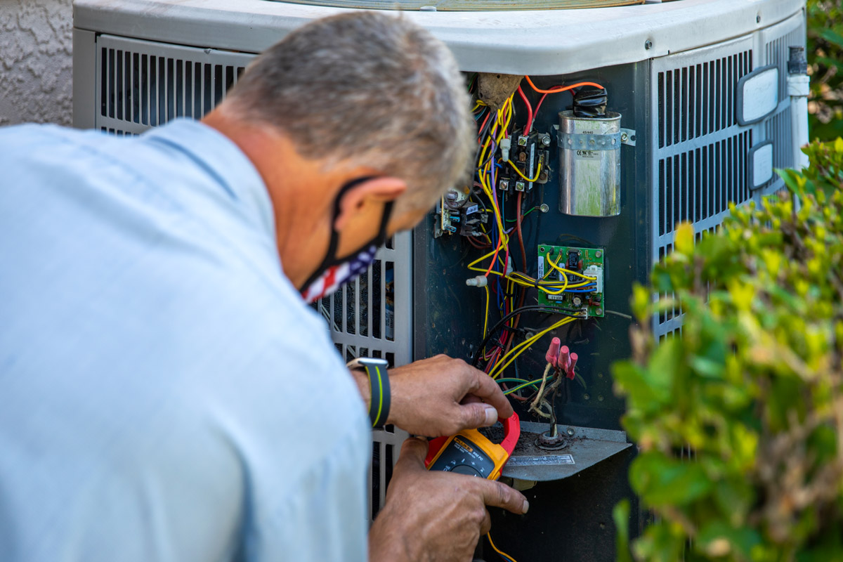 A man works on an outdoor a/c unit.