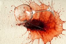 A glass of red wine spills on white carpet.