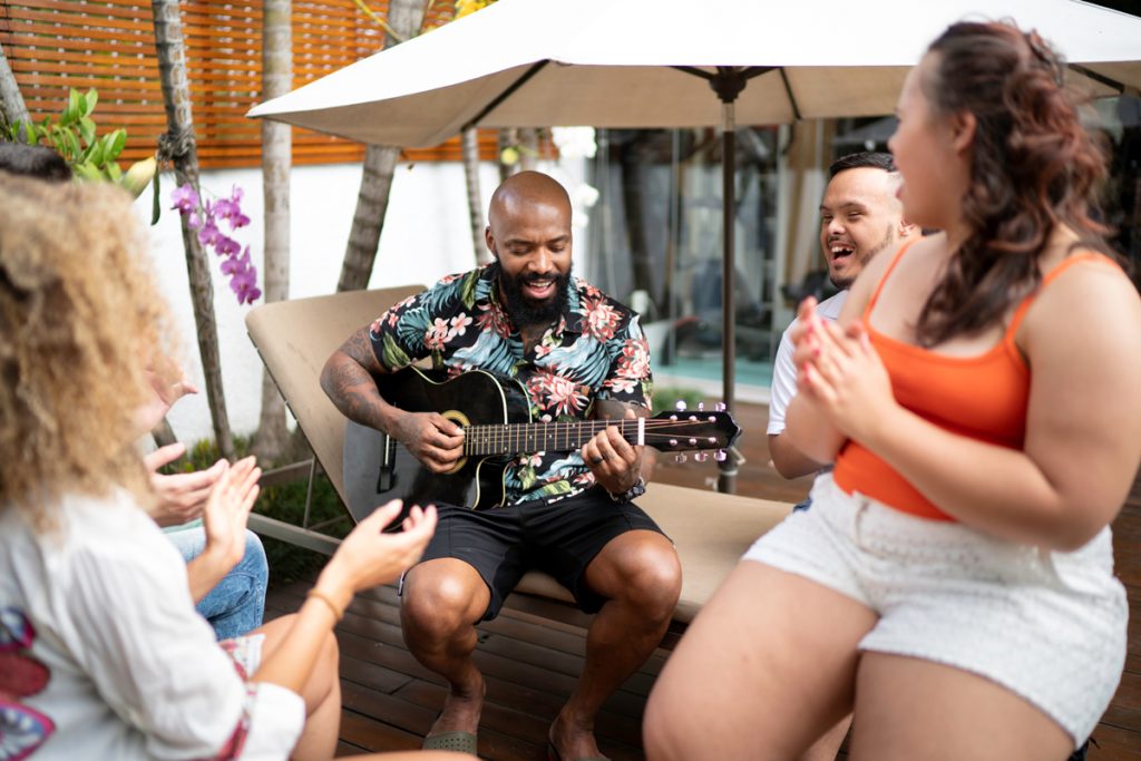 Friends listen to another friend playing guitar on a patio.