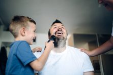 A father gets his beard shaved off by his two sons at home.