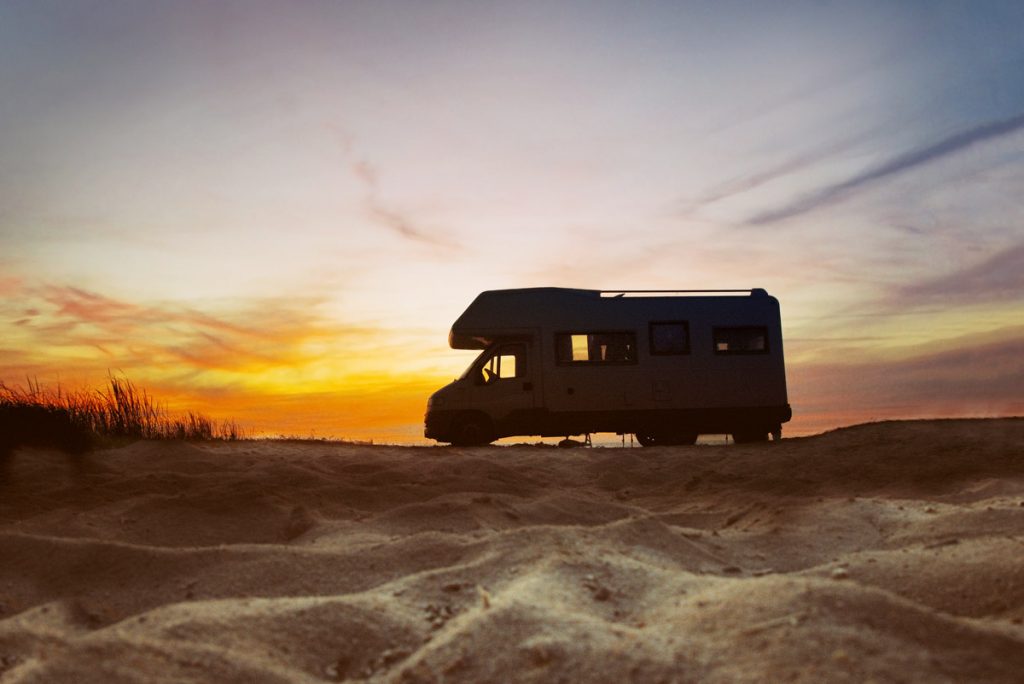 An RV rides along the road at sunset in the desert. 