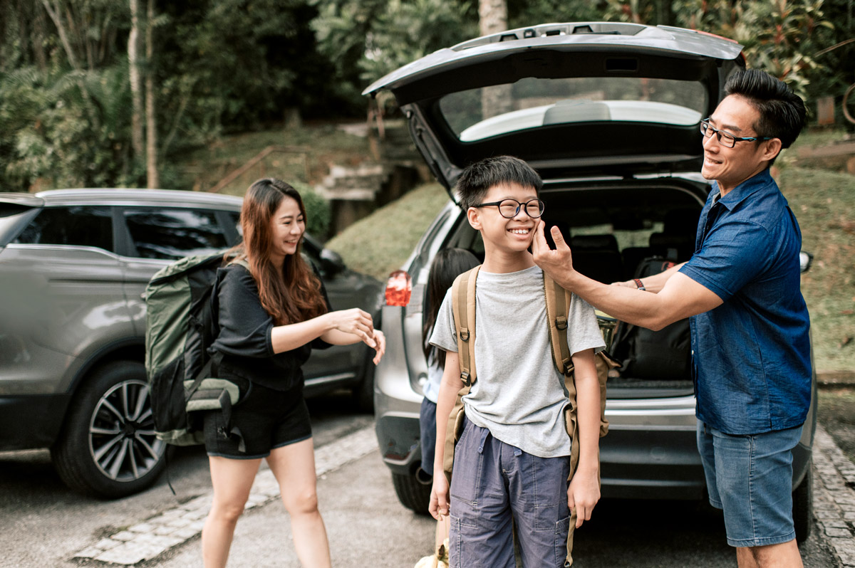 A father jokingly touches his son's cheek as they pack their vehicle for a road trip.