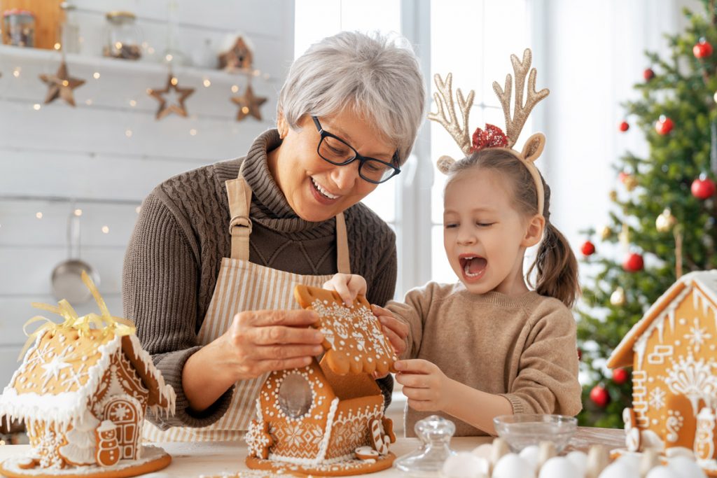 A grandmother and granddaughter build a gingerbread house together.