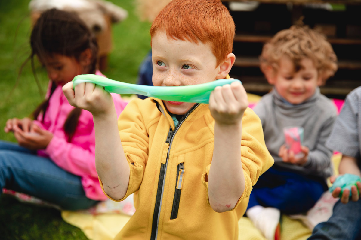 A little boy plays with green slime. He's wearing a yellow jacket.