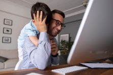 A man works from home as his son comes up behind him to give him a surprise hug.
