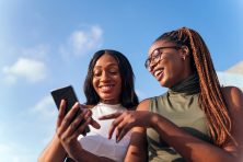 two women look at a phone and laugh