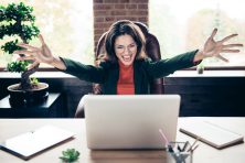 A woman looks thrilled as she looks at her laptop.