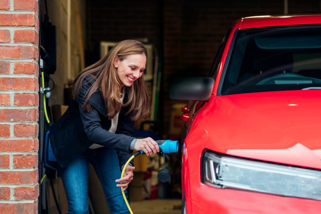 A woman charges her electric vehicle in the garage of her home.