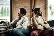 A married couple have a disagreement with their backs turned away from one another on their living room couch.