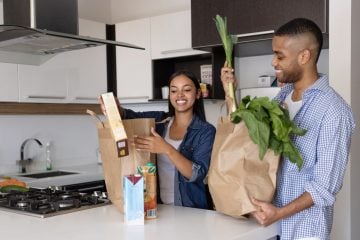 A couple unpack their groceries in their kitchen.