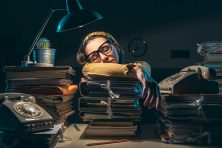 A woman sleeps at her desk surrounded by stacks of folders.