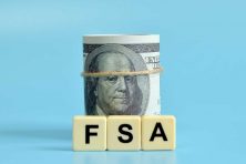 A stock image shows a roll of cash and the letters FSA, which is an abbreviation for Flexible Spending Account.