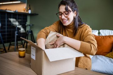 A woman smiles as she opens up a box. You could get free samples online delivered to you.