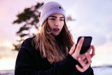 A woman looks upset as she looks at her phone with the sun setting in the background.