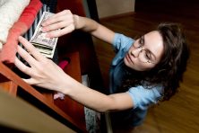 A woman stashes money away in a box underneath her clothes in her closet.