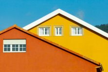 The upper level of two homes is shown against blue sky. The colors of the house include terracotta and yellow.