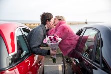 Two people on a date kiss while leaning out of their respective vehicles.