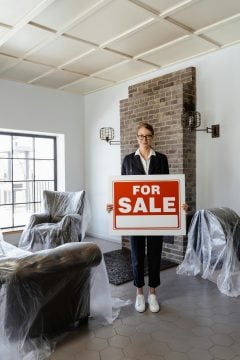 A woman holds a for sale sign among covered furniture. People often sell furniture on apps.