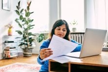 A woman files her taxes online while sitting on the floor in her living room. Her laptop is on her coffee table.
