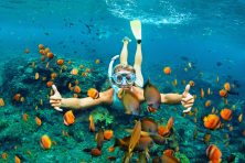 A woman snorkels with orange fish all around her in the ocean.