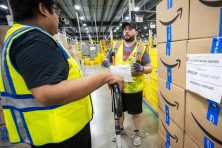 Two men talk while they are loading boxes onto a lift at an Amazon fulfillment center.