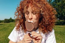 A woman eats a chocolate ice cream bar outside.