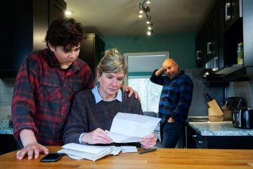 A son puts his arm around his mother's shoulder as they look at their credit card debt.