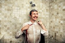 A man in a suit adjusts his tie in the shower.