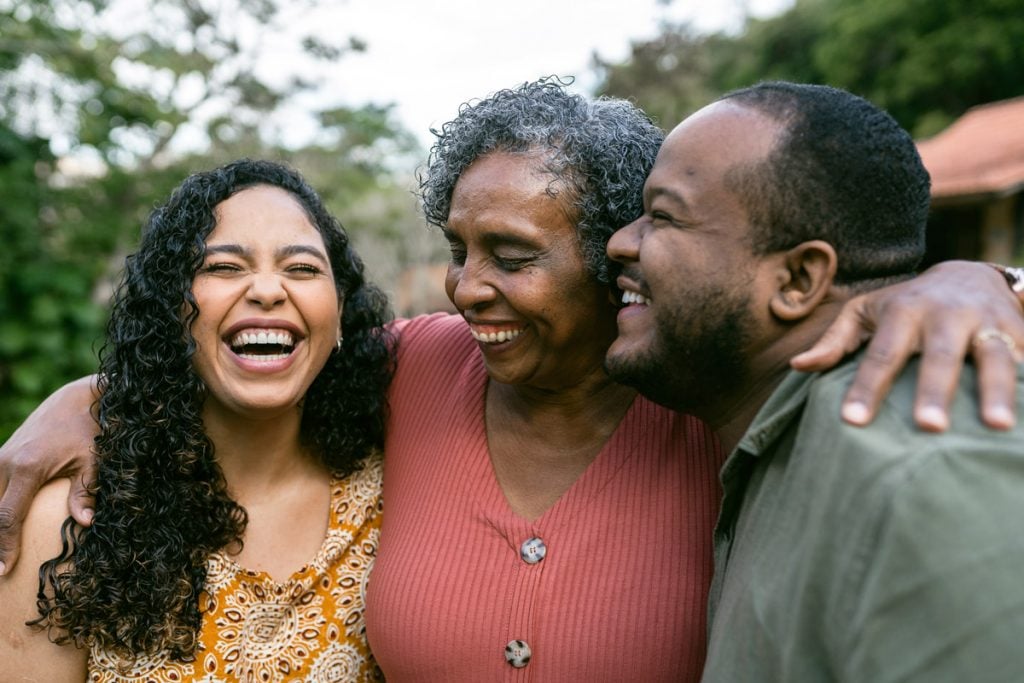 A mother spends time with her two adult children. They are laughing while hugging.